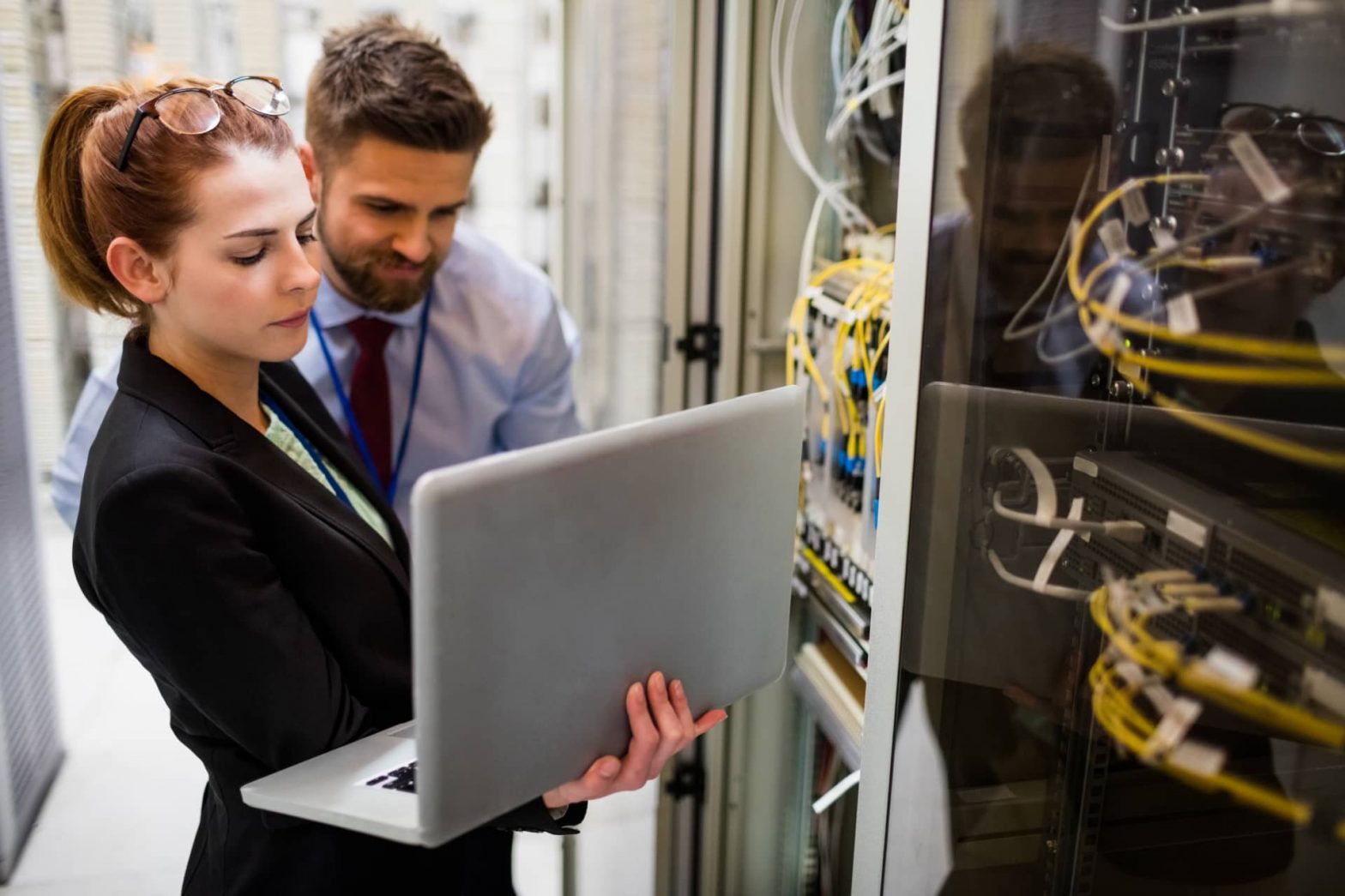 Woman holding laptop and man behind her looking at it in a server room